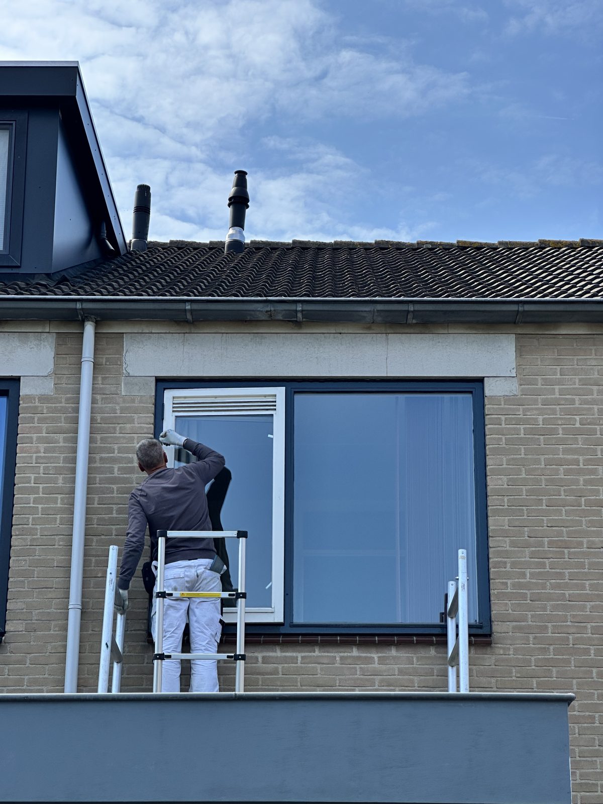 Ron up a ladder, painting an upstairs window frame